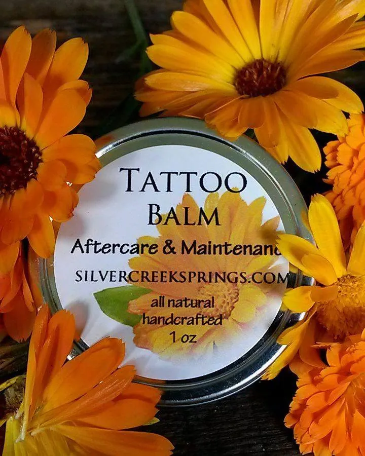 A tin of Tattoo Balm aftercare surrounded by calendula flowers